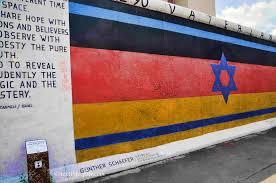 The East Side Gallery is an open-air gallery with a series of murals painted directly on a 1316 metre long remnant of the Berlin Wall, a fitting monument to the fall of the wall and the peaceful negotiation of borders and conventions between societies and people. The most famous image that appears on it is The Kiss which depicts Soviet leader Leonid Brezhnev giving the East Germany President Erich Honecker what appears to be a passionate kiss on the lips. Another famous image is a memorial to the Jewish citizens, The Vaterland, painted by Günther Schaefer, showing a Star of David over the German flag, which has been vandalized many times with anti-semitic graffiti. A youth-led campaign is underway to restore the memorial. Paint over Prejudice, an initiative organised by the FZY (Britain's Federation of Zionist Youth). They didn't want it to just be painted over again -- a protective glaze will mean if there is any further graffiti it can be washed off without damaging the original painting. Do you think it is important to preserve this wall and this gallery so that this part of history will never be forgotten, and never be repeated?