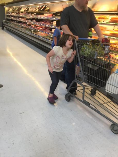 A woman was shopping in the store when she noticed the man pulling the girl in an odd way. It appeared her hair was wrapped around the handle of the cart, and he was holding her hair in place. She was walking very close to the cart with her head at an angle. The child was overheard saying, 