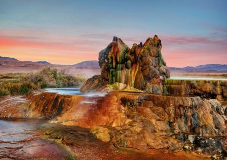 Fly Geyser located in Nevada on the edge of Black Rock Desert is actually man-made, by accident. It is shaped like a series of melting Hershey's Kisses. It was created accidentally in 1964 after a geothermal power company drilled a test well at the site. According to later newspaper reports, the well was either left uncapped or improperly plugged. Scalding hot water shot from the well hole and calcium carbonate deposits began to form, growing several inches each year. Those deposits have become three large mounds almost 6 feet tall and are brightly colored green and red. The 3 cones still spew scalding hot water about four or five feet into the air. According to scientists familiar with the geyser, the coloring is the result of thermophilic algae, which flourishes in moist, hot environments. Have you seen this unusual formation or any similar?